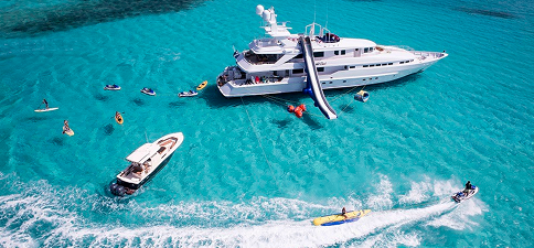 Luxury yacht anchored in clear water with water toys around it